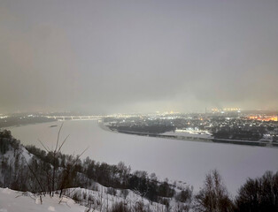Obraz premium Far view of the city and the frozen river with bridge on a foggy winter night in Nizhny Novgorod, Russia, January 6, 2022