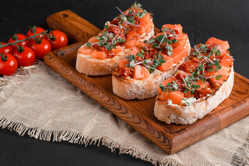 bruschetta with salmon, cottage cheese, dried tomatoes and micro greens, on a black background