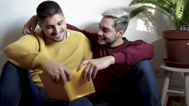 Lgbt gay couple hugging and reading book together indoor at home - Homosexual love and romance concept