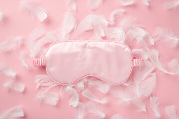 Top view photo of pink silk sleeping mask and feathers on isolated pastel pink background with...