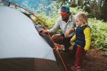 Selbstklebende Fototapeten Family camping outdoor child helps to set tent father and daughter travel together hiking vacations adventure lifestyle © EVERST
