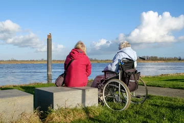 Fototapeten Caregiver next to woman in wheelchair on the banks of the IJssel near Hattem  Gelderland province, The Netherlands © Holland-PhotostockNL