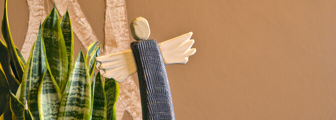 wooden painted angel with green plant on abstract blurry background, old handicraft figurine,...