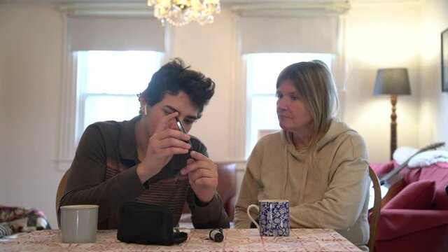 A diabetes patient testing his blood sugar at home with the support of his mother
