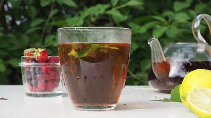 Pouring tea from a teapot into a cup on a blurred background of nature. nearby is lemon and lemongrass, wild berries. pour boiling water into a kettle to make herbal tea