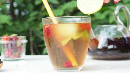 Iced fruit tea or cold berry drink in clear glass with mint leaf. fresh berries raspberries, blueberries, strawberries, lime. Refreshing summer drink. nature foliage background