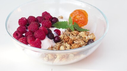 eat proper nutrition and healthy breakfast bowl of oat granola with yogurt, fresh raspberries, blueberries, strawberries, blackberries and nuts with spoon on white for healthy breakfast, top view