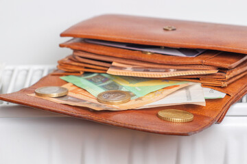 Expensive heating costs. Paying bills. Open wallet with Euro money banknotes on heating radiator battery at home