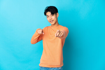 Young Chinese man isolated on blue background pointing front with happy expression