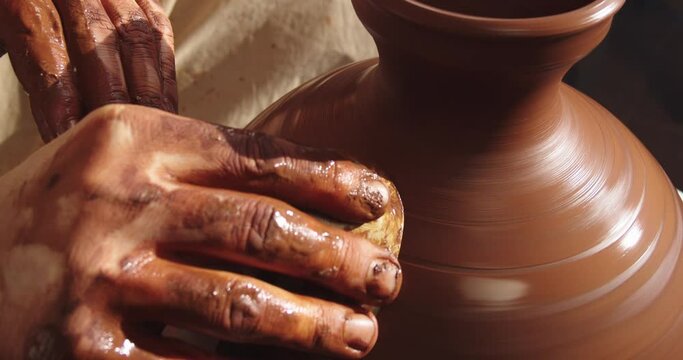 A clay pot spinning on a potter's wheel and trimmed by a potter
