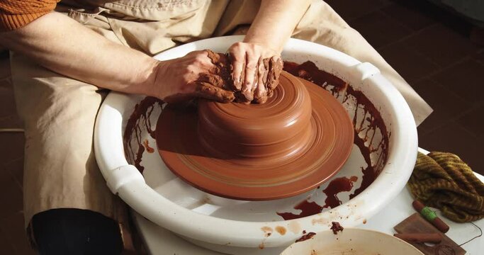 A potter makes a clay pot on a potter's wheel. Hands of the hands are shown in close-up. Handmade ceramics manufacturing process.