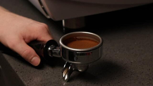 Closeup of barista hands using tamper to press ground coffee into portafilter to make espresso hot drink.