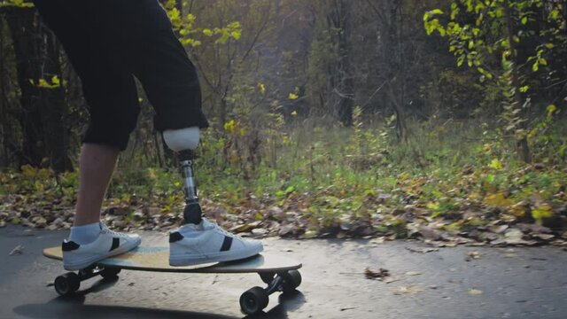 A young man with a metal prosthetic leg rides a skateboard in an autumn park. Go in for sports with an artificial leg. a11y