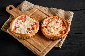 Two delicious pizzas on a cutting board on a black wooden background. Rustic style.