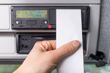 Close up of a driver holding empty printed day shift in focus against a digital tachograph in...