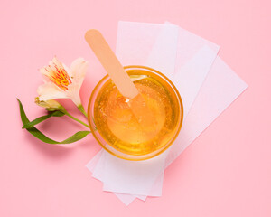 Liquid yellow sugar paste, wooden spatula, flower and depilatory strips on a pink background....