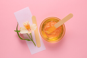 Liquid yellow sugar paste, wooden spatula, flower and depilatory strips on a pink background. Removing unwanted hair. Sugaring.Depilation. Epilation. Beauty. - obrazy, fototapety, plakaty