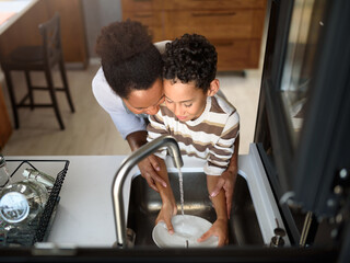 Son is helping mother in the Kitchen, Washing Dishes. African American family. - Powered by Adobe