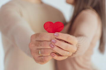 Unrecognizable couple in love embracing while holding a small red heart in their hands.