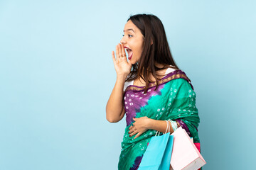 Young Indian woman with shopping bags shouting with mouth wide open to the side