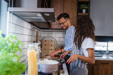 Young cheerful multi-ethnic couple preparing tomato pasta together at home kitchen