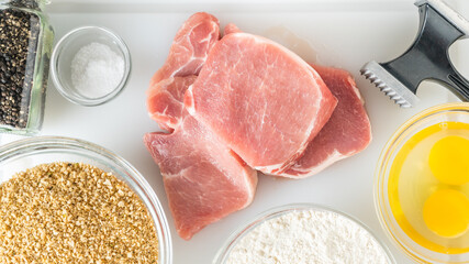 Breaded pork chops recipe. Raw pork chops, eggs, flour, bread crumbs, salt and black pepper close up, flat lay