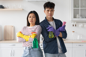Serious asian man and woman with cleaning sprays and sponges