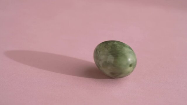Jade egg spinning on pink background, slow motion
