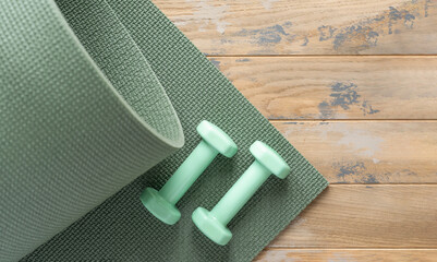Green dumbbells and the green sports mat on the wooden floor - obrazy, fototapety, plakaty