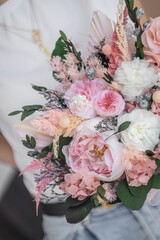 A beautiful summer bouquet in the hands of a girl. Bouquet of spray roses, peonies and French roses in white-pink tones.