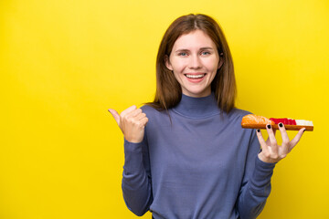 Young English woman holding sashimi isolated on yellow background pointing to the side to present a product