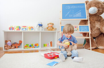 Cute child boy in home quarantine playing doctor with toys wearing medical masks, role playing during coronavirus pandemic lock down