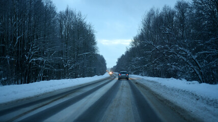 Winter. The car drives along the road with a turn through the forest. Snow-covered trees bent over the road. © Nadezda