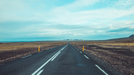 Amazing view of the asphalt road in iceland, leading towards mountains. Leading lines towards lonely mountains in solitude and thick clouds above.