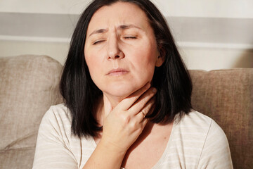 Fototapeta premium Mature woman touching her neck. Sick woman feels sore throat, cough, pharyngitis and hoarseness. Thyroid disorder. Medical and health care.
