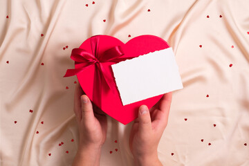 Man's hands hold a heart-shaped box with candy and a blank card over a silk background. Happy...