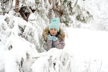 Fototapeta na wymiar A girl in warm winter overalls on a walk in the winter forest: active games, playing snowballs and other activities