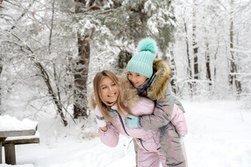 Mom and daughter in warm winter overalls for a walk in the winter forest: active games, playing snowballs and other activities