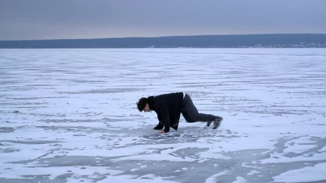 The guy walks on the frozen ice of the river and slips and falls. Winter season. Side view.