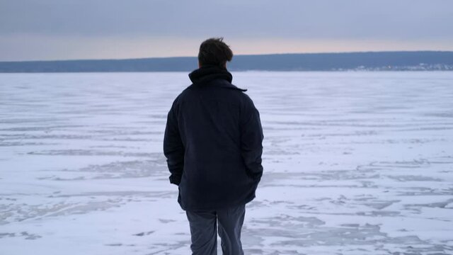 A young guy walks on a frozen lake alone. Winter season.