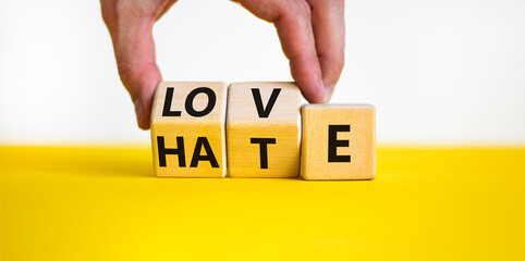 From hate to love symbol. Man turns wooden cubes and changes the word hate to love. Beautiful yellow table, white background, copy space. Valentines day and hate or love concept.