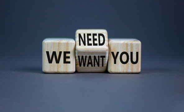 We want and need you symbol. Businessman turns the wooden cube and changes words we want you to we need you. Beautiful grey background, copy space. Business, support we want and need you concept.