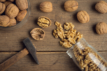 Nuts coming out of a glass jar and hammer on a wooden table in a dark environment.. High quality photo