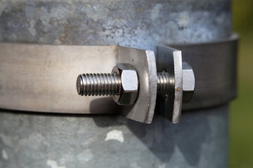 Grey metallic rainwater pipe attached to a building with a metal ring that is bolted around it. Closeup color image of the bolt and the pipe during a sunny spring day in Finland.