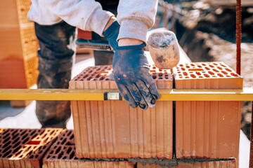 Bricklayer industrial worker installing brick masonry on exterior wall using level and rubber hammer