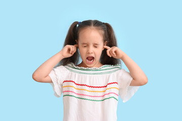 Emotional little girl with ponytails closing ears on blue background