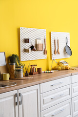 Peg boards with kitchenware hanging on yellow wall