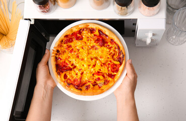 Woman putting plate with pizza into microwave oven in kitchen, closeup
