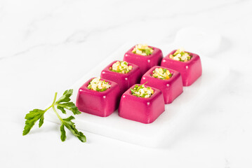 Obraz na płótnie Canvas Appetizer Beetroot cream jelly in the form of small portions of a square shape with a filling of finely chopped egg with parsley on a serving board on a white background