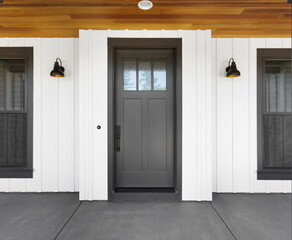 Front door to new luxury modern farmhouse style home: black front door with white vertical siding and sconce lights. Upper portion of door has glass with mullions.